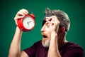 Surprised man in red t-shirt and sleep mask on head holding alarm clock. Lifestyle and bed time concept Royalty Free Stock Photo