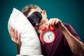 Surprised man in red t-shirt and sleep mask on head holding alarm clock and pillow. Lifestyle and bed time concept Royalty Free Stock Photo