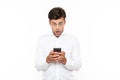 Surprised man with short dark hair chatting or typing text message using cell phone, isolated over white background Royalty Free Stock Photo