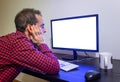 Surprised Man Stares at Office Computer on Wooden Black Desk Mockup. Dotted Red Shirt, LCD Screen, Keyboard, Mouse, White Mug. Royalty Free Stock Photo