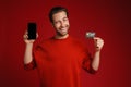 Surprised man winking while showing credit card and cellphone