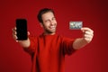 Surprised man winking while showing credit card and cellphone