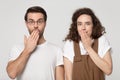 Surprised millennial joyful shy couple covering mouths with hands.
