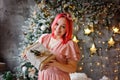 A surprised model girl with pink hair and a dress holding a gift box and posing near a Christmas tree. A young beautiful woman Royalty Free Stock Photo