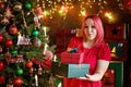 A surprised model girl with pink hair and a dress holding a gift box and posing near a Christmas tree. A young beautiful woman Royalty Free Stock Photo