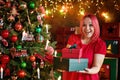 A surprised model girl with pink hair and a dress holding a gift box and posing near a Christmas tree. A young beautiful woman Royalty Free Stock Photo