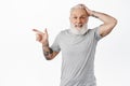 Surprised old guy pointing left and touching head, smiling amazed, encounter something interesting, have you seen it Royalty Free Stock Photo