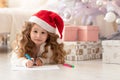 Surprised, pensive, little girl in red hat writing a letter to santa claus Royalty Free Stock Photo