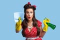 Surprised pinup lady in retro clothes cleaning screen with rag, using spray detergent on blue studio background