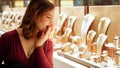 Surprised pretty woman looking at jewelry in store window. Girl near jewellery. Interested customer chooses gold, diamonds or