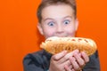 Surprised puffy eyes 10s boy wants to bite a big hot dog.Closeup orange studio background