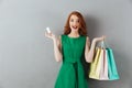 Surprised redhead young woman holding shopping bags and credit card. Royalty Free Stock Photo