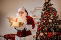 Surprised Santa Claus with a magical glowing gift near beautiful christmas tree. New year and Merry Christmas , happy holidays