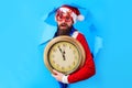 Surprised Santa man with vintage clock looking through paper hole. Prepare to Christmas or New year. Royalty Free Stock Photo