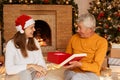 Surprised senior man wearing orange sweater opening present box from his daughter, expressing astonishment, posing near Christmas Royalty Free Stock Photo