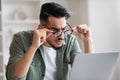 Surprised serious young arab man with beard takes off his glasses looks at laptop in home office interior Royalty Free Stock Photo