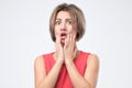 Surprised shocked female wearing red dress r, keeping her hand on cheek, opening mouth. Royalty Free Stock Photo