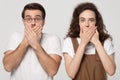 Surprised shocked millennial couple covering mouths with hands.