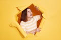 Surprised shocked young adult woman stands in torn paper hole, looking aside with open mouth and amazed facial expression, looking Royalty Free Stock Photo