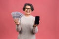 Surprised smiling happy senior mature aged senior woman in casual showing blank smartphone screen isolated over pink background. Royalty Free Stock Photo