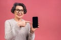 Surprised smiling happy senior mature aged senior woman in casual showing blank smartphone screen while looking at the camera Royalty Free Stock Photo