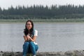 Surprised sports Yakut Asian with glasses young girl sitting on the old pier of the river Viluy in the Northern taiga firs