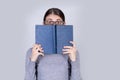 Surprised student girl with glasses covering half face with a opened blue book . Stunned emotive young woman looking amazed Royalty Free Stock Photo