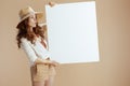 surprised stylish woman showing blank board isolated on beige