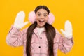 surprised teen girl in winter mittens and earmuffs on yellow background, winter fashion Royalty Free Stock Photo