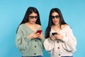 Surprised twin girls in 3D glasses with smartphones on a blue background.