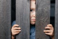 Surprised white boy looks out of the crack of a wooden fence. Childish curiosity. Espionage. Rural life. Child Royalty Free Stock Photo