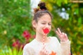 Surprised winking little Girl holding funny lips on stick and showing victory gesture on green nature background.