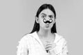 Surprised winking model Girl holding funny mustache on stick and showing empty copy space on open hand palm for text Royalty Free Stock Photo