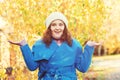 Surprised woman at autumn park, presenting something on empty palms. Autumn season. Woman in blue coat and knitted hat enjoying au