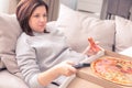 Surprised woman eating pizza and watching TV with remote control at home, warm tone Royalty Free Stock Photo