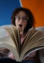 Surprised woman with glasses and curly hair looking through the moving pages of an open book Royalty Free Stock Photo