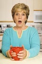 Surprised woman holding coffee mug in kitchen