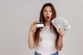 Surprised woman holding fan of dollars banknotes and credit card, pondering deposit percentage, Royalty Free Stock Photo
