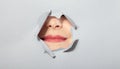 Surprised woman looking playfully in torn paper hole, has excited cheerful expression, looks through breakthrough of Royalty Free Stock Photo