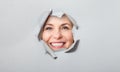 Surprised woman looking playfully in torn paper hole, has excited cheerful expression, looks through breakthrough of Royalty Free Stock Photo