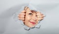 Surprised woman looking playfully in torn paper hole, has excited cheerful expression, looks through breakthrough of gray Royalty Free Stock Photo