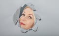 Surprised woman looking playfully in torn paper hole, has excited cheerful expression, looks through breakthrough of gray Royalty Free Stock Photo