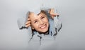 Surprised woman looking playfully in torn paper hole, has excited cheerful expression, looks through breakthrough of gray Royalty Free Stock Photo