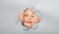Surprised woman looking playfully in torn paper hole, has excited cheerful expression, looks through breakthrough of gray Royalty Free Stock Photo