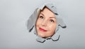 Surprised woman looking playfully in torn paper hole, has excited cheerful expression, looks through breakthrough of gray Royalty Free Stock Photo