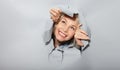 Surprised woman looking playfully in torn paper hole, has excited cheerful expression, looks through breakthrough of gray Royalty Free Stock Photo