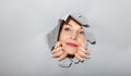 Surprised woman looking playfully in torn paper hole, has excited cheerful expression, looks through breakthrough of gray Royalty Free Stock Photo