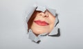 Surprised woman looking playfully in torn paper hole, has excited cheerful expression, looks through breakthrough of gray Royalty Free Stock Photo