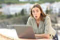 Surprised woman looks at camera using laptop in a balcony Royalty Free Stock Photo