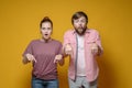 Surprised woman and man point down with their index fingers and stare wide-eyed at the camera, on a yellow background. Royalty Free Stock Photo